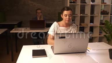 美丽的白种人同事女孩，坐在笔记本电脑前，打字专注，工作情绪，办公室砖
